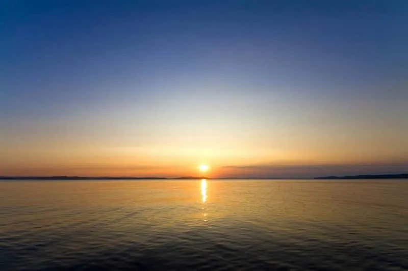 Small group of travellers on a sailboat deck watching sunset over the Aegean Sea on a Mykonos island nightlife cruise